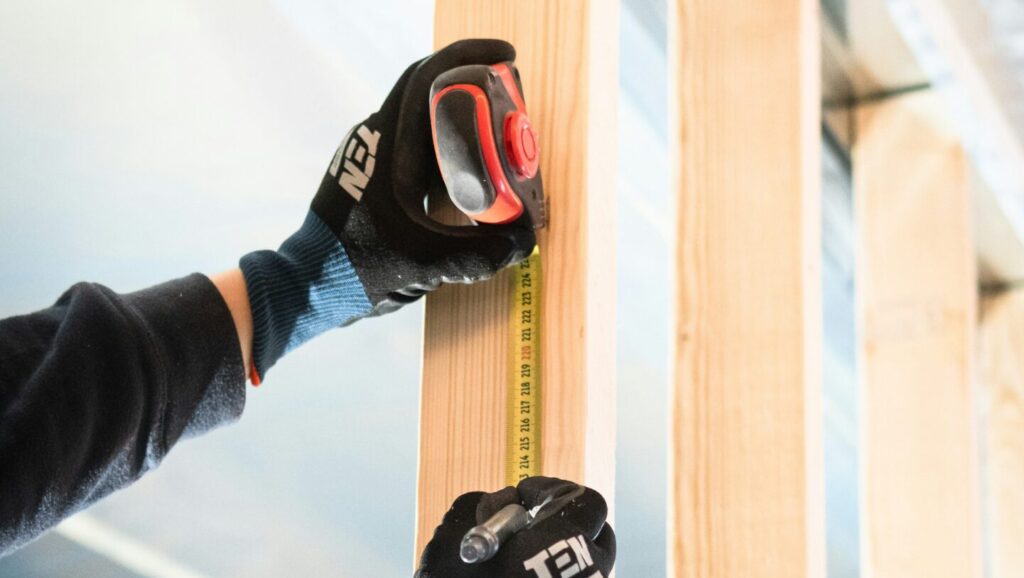 Obrázek zobrazuje ruce v rukavicích, které drží manuální metr