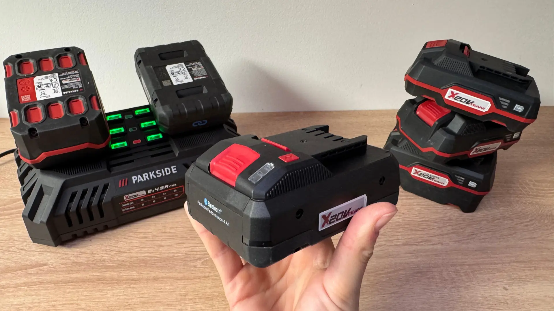 Akumulátor Parkside X20V v ruce před dvojitou nabíječkou Parkside s rozsvícenými kontrolkami