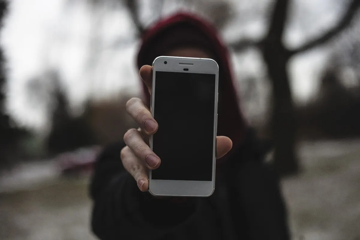 Postava v kapuci drží mobilní telefon