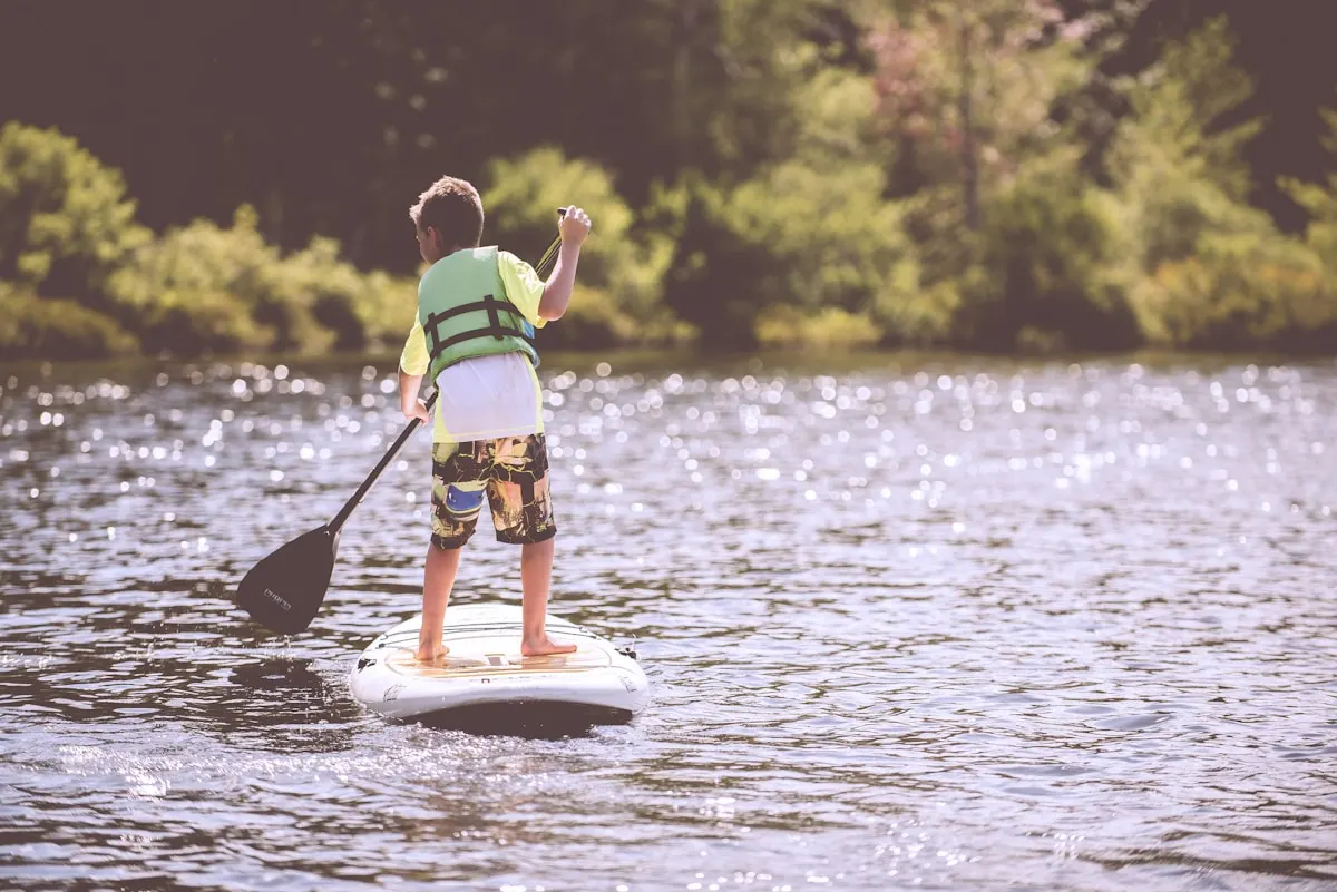 Chlapec v plovací vestě pádluje na paddleboardu
