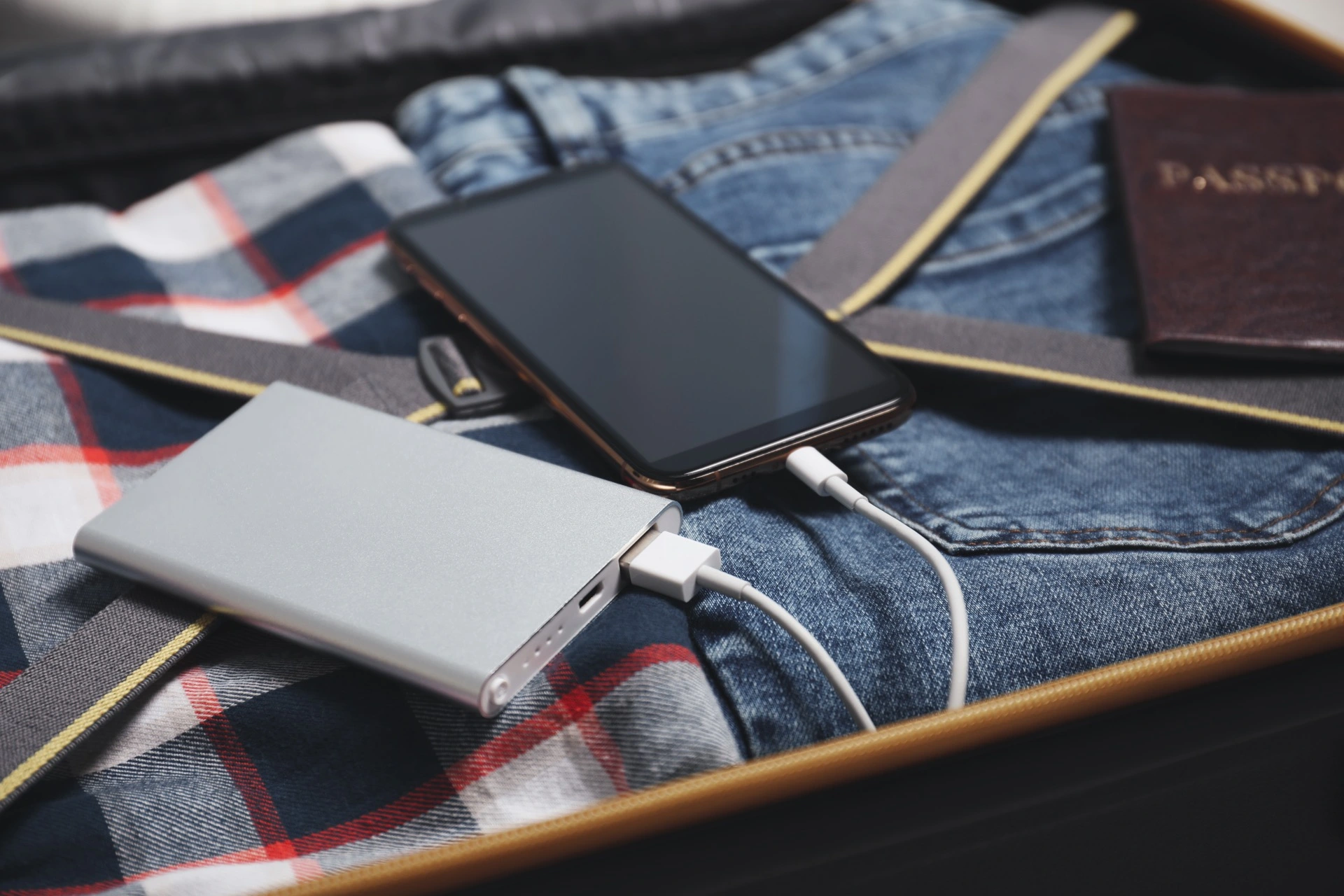 Powerbanka a telefon v otevřeném zavazadle vedle cestovního pasu