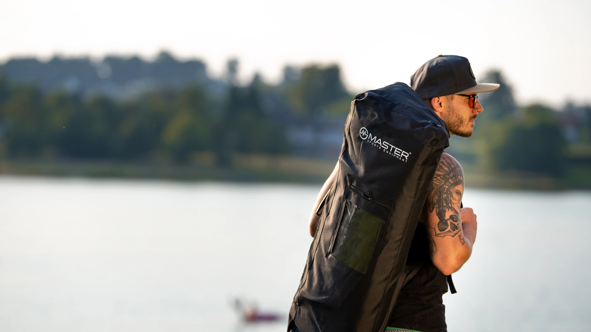 Muž nese na zádech přepravní batoh s paddleboardem Master Aqua Sturgeon u jezera