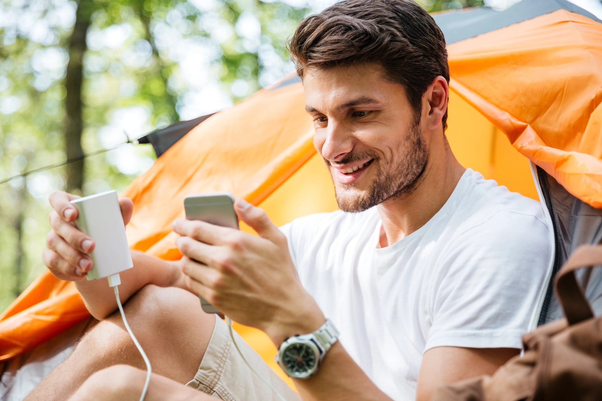 Nabíjení telefonu z powerbanky u stanu v přírodě