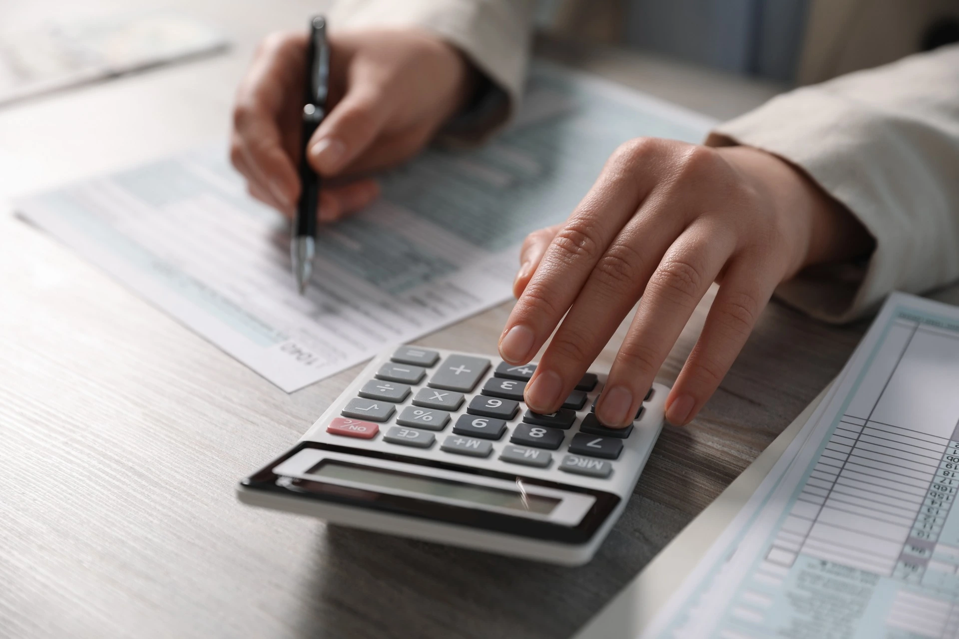 Ruce při kontrole dvou dokumentů s kalkulačkou.