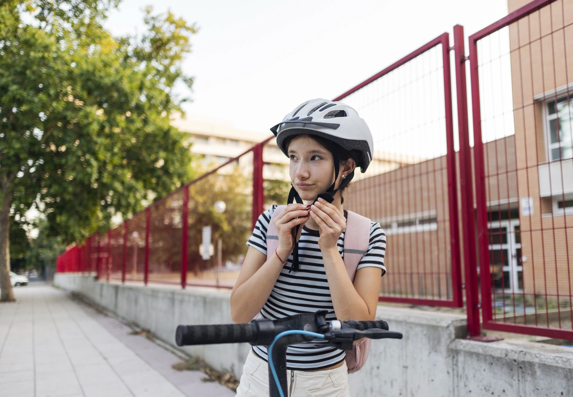 Dospívající dívka si zapíná cyklistickou přilbu u elektrokoloběžky