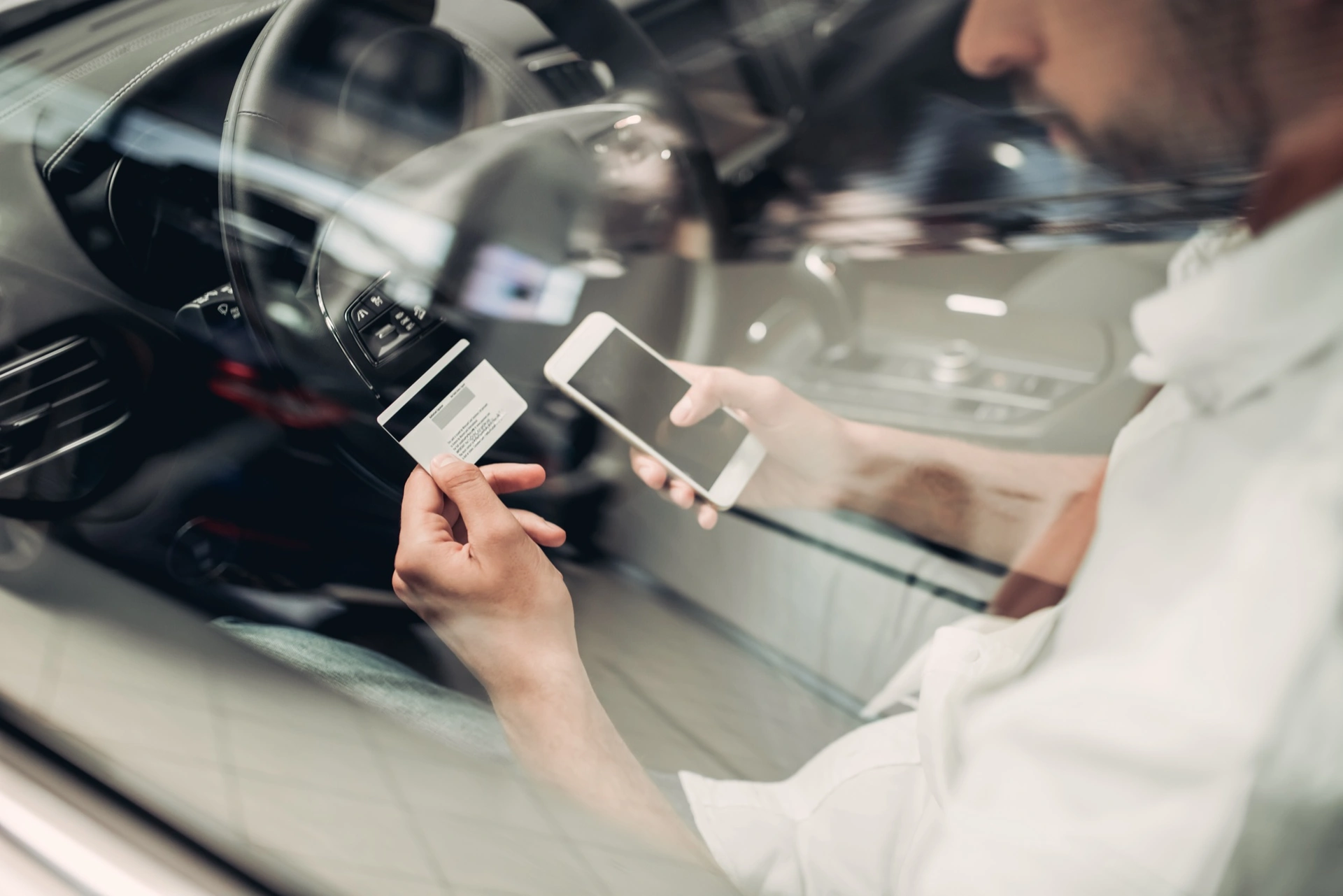 Řidič v autě drží platební kartu a mobilní telefon