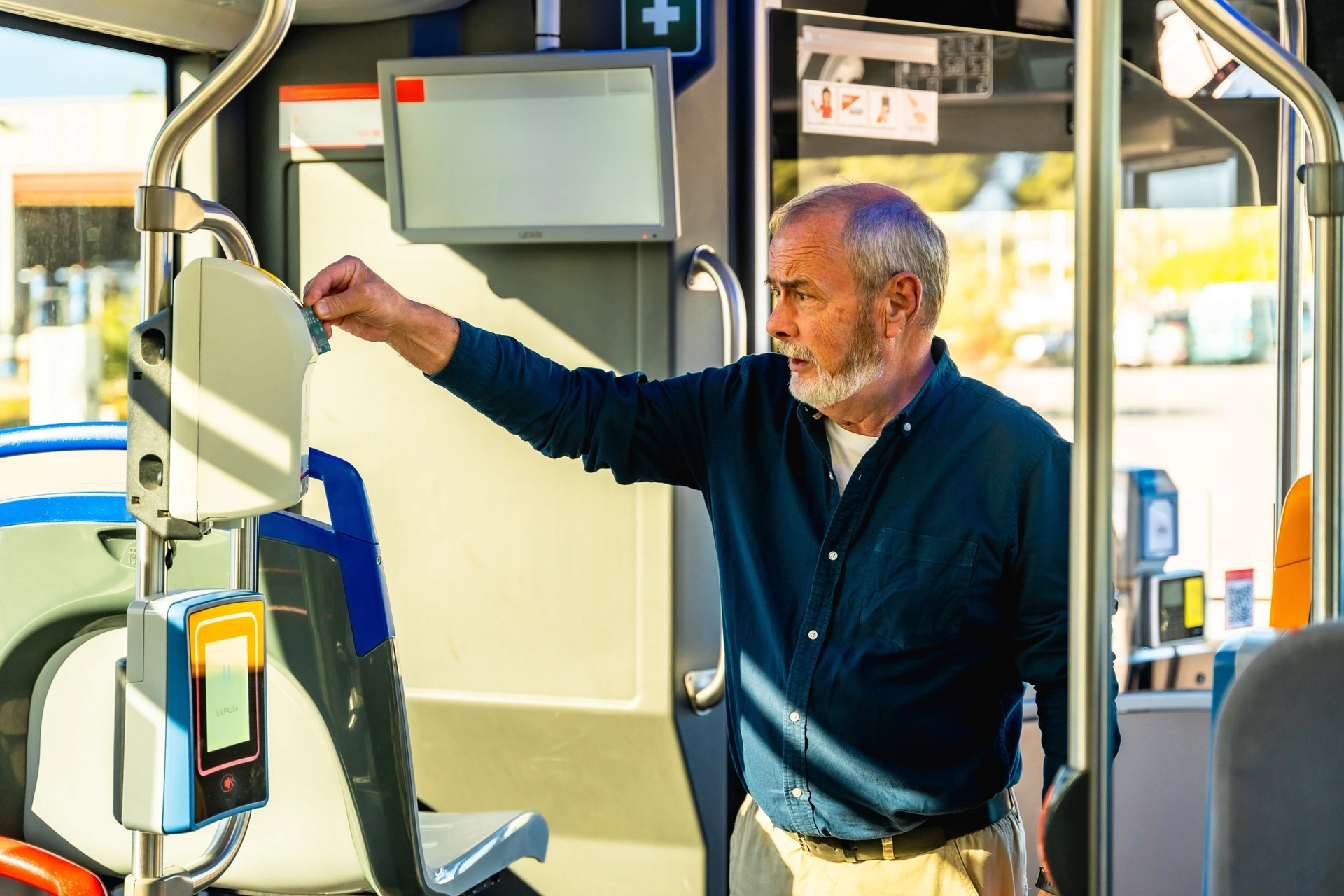 Starší muž přikládá jízdenku ke čtečce v autobusu městské dopravy