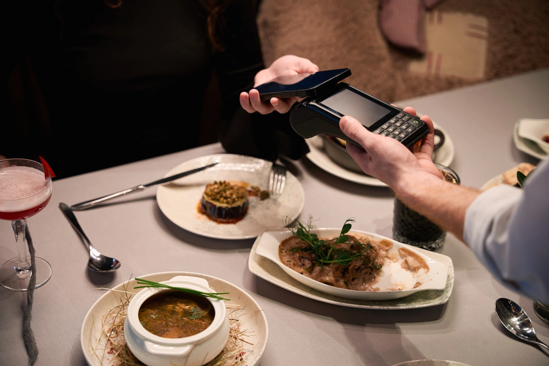 Obsluha podává platební terminál hostovi u stolu v restauraci