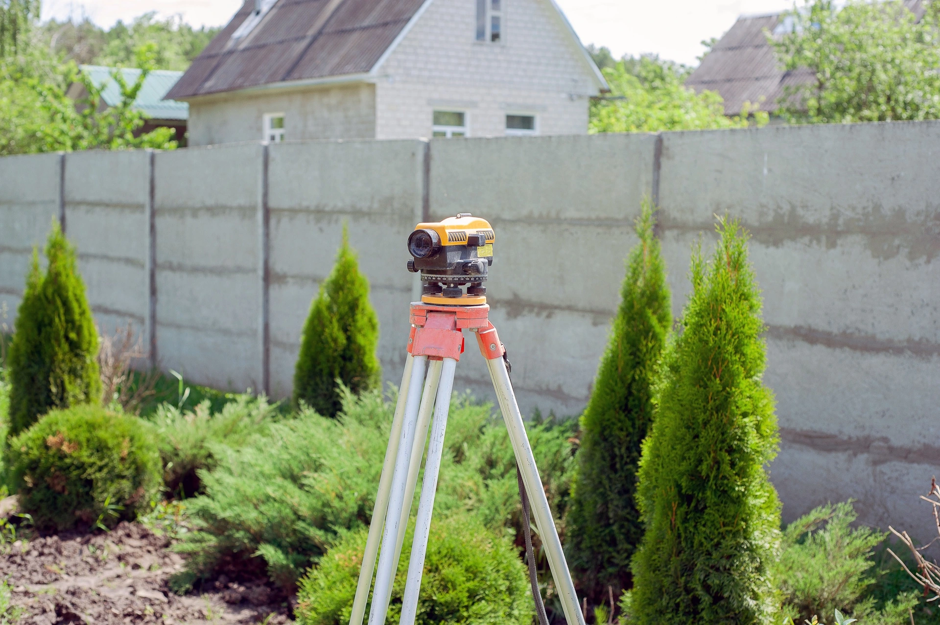 Měřicí přístroj geodeta na stativu na zahradě před betonovým plotem