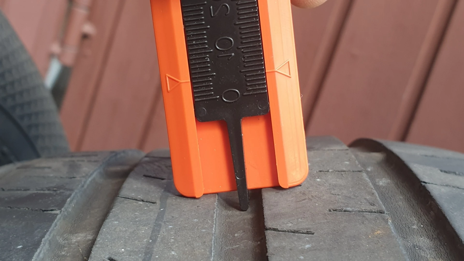 Oranžový hloubkoměr zasunutý do drážky ojeté pneumatiky.