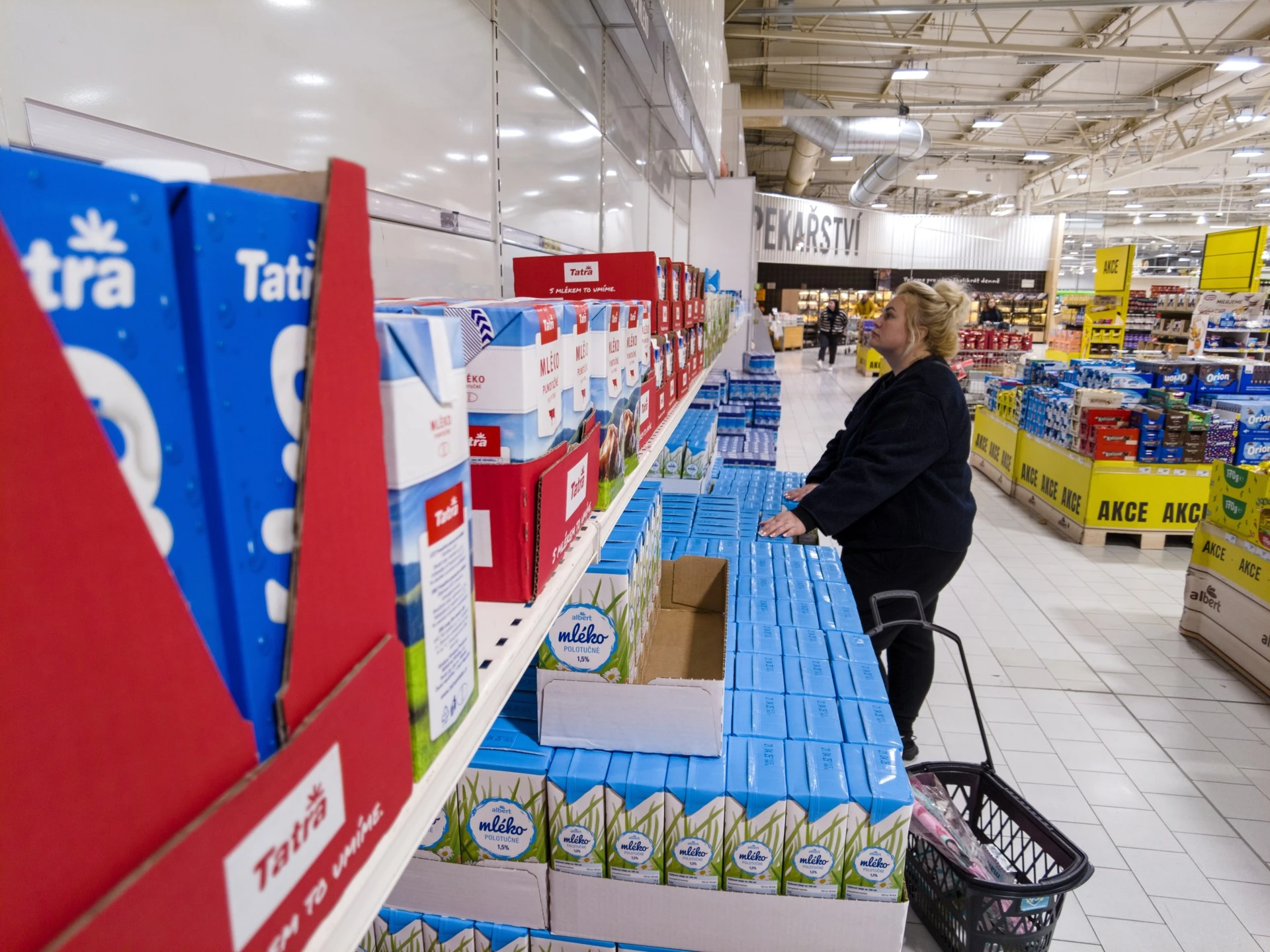 Zákaznice s nákupním košíkem u regálu s mlékem v hypermarketu.