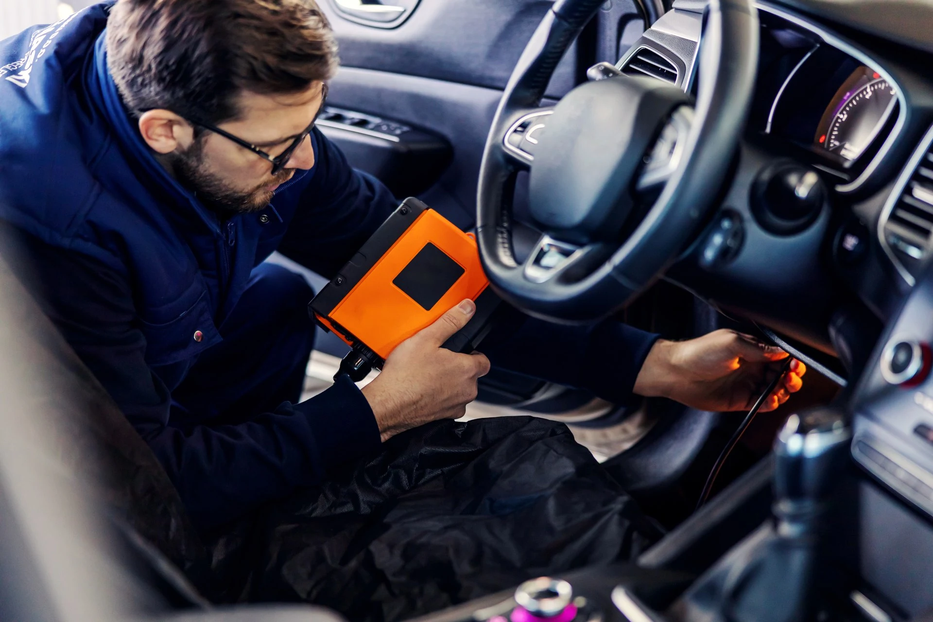 Technik připojuje diagnostický přístroj do zásuvky pod volantem osobního auta.